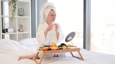 Kafkasyalı rahat bir kadın sabah banyodan sonra altın maskeler takarken makyaj aynasına ev yapımı spa malzemeleriyle bakıyor. Güzel bayan sabahları yatak odasında cilt bakımını yapıyor..