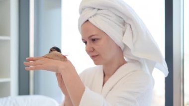 Kafasında banyo havlusu olan beyaz kadın, arka planda bir elden diğerine sürünen büyük salyangoza bakıyor. Güzel bir kadın hafta sonu tatlı bir hayvanla güzellik terapisinden zevk alıyor..