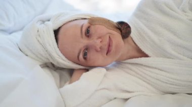 Tatlı yumuşakça yüzünde sürünürken, genç bir bayanın yatakta gözleri kapalı yatışının yakın görüntüsü. Yumuşak havluyla çekici bir bayan yatakta hafif masajdan sonra salyangoz yüz prosedürünün tadını çıkarıyor..