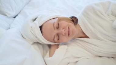Kafasında banyo havlusu olan güzel bir kadının, yumuşak bir battaniyenin üzerinde yatarken yüzünde sevimli bir salyangoz tutuşu. Huzurlu genç yetişkin cilt üzerinde iyileştirici sümük kullanarak kozmetoloji tedavisi görüyor..