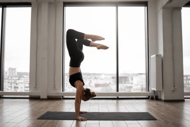 Kadın yogi, özel bir stüdyoda yoga yaparken amuda kalkıyor. Siyah taytlı genç bir kadın spor şiltelerini antrenman için kullanıyor. Zihin ve vücut bakımı kavramı.