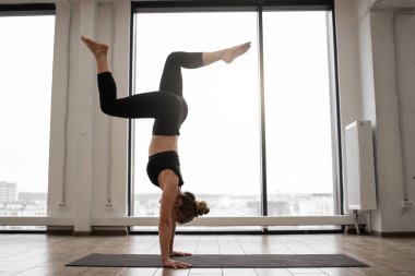 Kadın yogi, özel bir stüdyoda yoga yaparken amuda kalkıyor. Siyah taytlı genç bir kadın spor şiltelerini antrenman için kullanıyor. Zihin ve vücut bakımı kavramı.