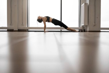Kafkasyalı genç bir kadın yoga minderinde yukarı doğru çıkıyor. Spor kıyafetleri üzerinde aktif kadın yogi Purvottanasana Poz çalışıyor Panoramik pencereli hava odasında.