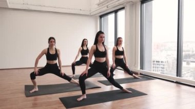 Bir grup siyah spor giyim giymiş genç sporcu stüdyoda yoga antrenmanı sırasında etkin bir eğitmenin rehberliğinde kaslarını esnetiyorlar. Çekici, zayıf kadınlar evde duygusal stresi azaltıyor..