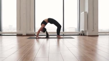 Siyah spor kıyafetli beyaz yogi Urdhva Dhanurasana pozu veriyor. Aktif bir kadın, yoga minderinin üzerinde Fransız pencereli briç egzersizi yapıyor..