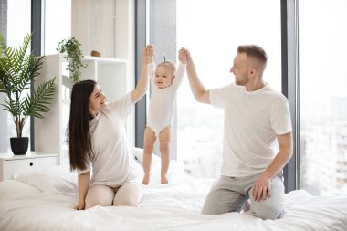 Keyifli aile üçlüsünün portresi günlük kıyafetlerle bebeği kollarıyla kaldırıyor ve şefkatle ona bakıyor. Sevgili karı koca, küçük kızlarıyla rahat evlerinde vakit geçirmenin keyfini çıkarıyorlar..