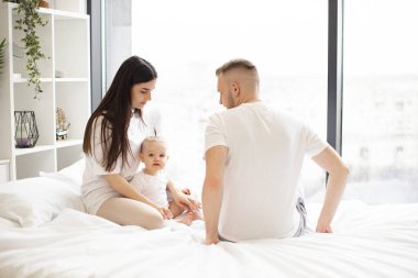 Sevimli küçük kız hafta sonu boyunca sevgi dolu anne babasıyla birlikte yatak odasındaki yumuşak yorganın üzerinde oturuyor. Neşeli beyaz anne ve baba evde dinlenirken güzel kızlarına bakıyorlar..