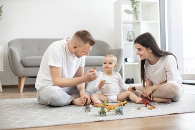 Genç, evli bir çift oturma odasında bacak bacak üstüne atarak oturuyor ve halının üzerinde küçük bir kızla dinozor oyunu oynuyorlar. Üç kişilik sevgi dolu aile evde birlikte vakit geçiriyorlar..