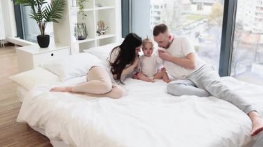 Mutlu, sevecen bir aile, kral yatağında uzanıyor ve beyaz, görkemli bir odada panorama manzaralı sevimli bir kıza sarılıyor. Genç baba tatlı kızını öperken anne nazikçe dokunuyor..