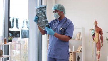 Koruyucu giysili çok ırklı dikkatli bir adam elinde hastane muayene odasında kalırken vücut parçalarının detaylı tomografisini tutuyor. Test sonuçlarına göre tıbbi pratisyen hekim hastalıkları teşhis ediyor.