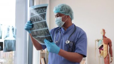Koruyucu giysili çok ırklı dikkatli bir adam elinde hastane muayene odasında kalırken vücut parçalarının detaylı tomografisini tutuyor. Test sonuçlarına göre tıbbi pratisyen hekim hastalıkları teşhis ediyor.