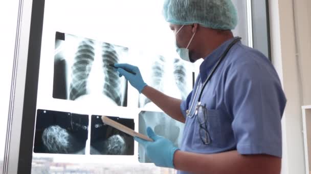 スタイラスペンでタブレットを使用して保護服で多人種医療従事者によって研究胸部X線検査に焦点を当てます 技術を用いて左肺の質量を識別する男性放射線医 — ストック動画