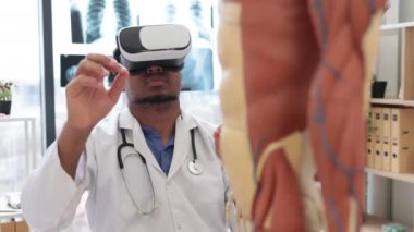 Laboratuvar önlüğü ve 3D gözlük takan Afro-Amerikan adam modern cihazlar ve insan iskeletinin yanında otururken VR sistemi kullanıyor. Eğitim hastanesinde tıbbi eğitime hazırlanan bir terapist..
