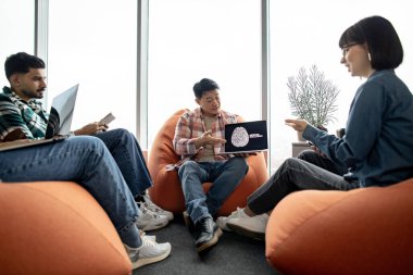 Bir grup çok ırklı iş arkadaşı iş yerinde sohbet ederken odaklanmış Asyalı adam bilgisayar ekranını işaret ediyor. Gelişigüzel çalışan akıllı veri bilimcileri makine zekasıyla iş operasyonlarını geliştiriyor.