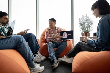 Çekici Asyalı bir erkeğin dizüstü bilgisayarını tutarken, beyaz bir kadının da ortak çalışma alanında parmaklarıyla yapay zeka resmi göstermesi. Günlük kıyafetlerini giymiş veri mühendisleri siber güvenlik geliştiriyor..