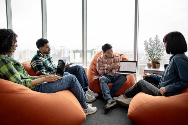 Çeşitli iş adamları modern aletlerle terracotta armut çantalarında otururken Asyalı adam çalışma alanında dizüstü bilgisayar gösteriyor. Veri analistleri proje istatistikleri hakkında beyin fırtınası yapıyorlar.