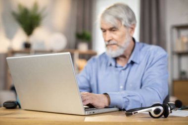 İş hayatında gülümseyen, gri saçlı bir erkek, evden uzakta çalışırken taşınabilir bilgisayarda daktilo kullanıyor. İçerideki internet bağlantısını kullanarak bilgi arayan deneyimli girişimci.