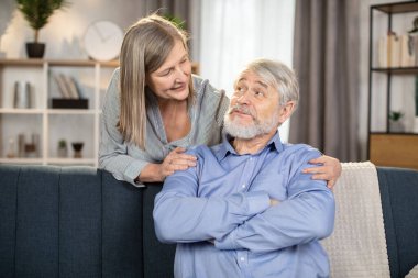 Günümüz stüdyo dairesinde birlikte vakit geçirmeyi seven aile babası ve karısının portresi. Orta yaşlı neşeli bayan kanepede otururken sıcak bir şekilde mutlu adama sarılıyor..
