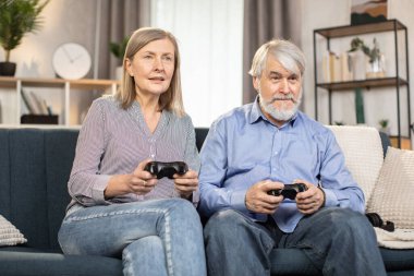 Yetişkin bir erkek ve kadın, evde konsolda oynarken ellerinde siyah oyun bloknotları tutuyorlar. Gündelik giysiler içinde duygusal evli bir çift video eğlencesinin başarılı sonuçlarından zevk alıyorlar..