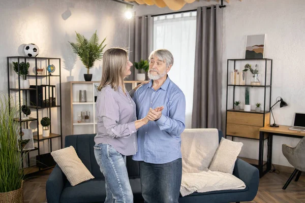 Sıradan kıyafetler giymiş, evde romantik müzik eşliğinde dans eden olgun bir çift. Sadık ortaklar evlilik yıldönümünü kutluyor. Koşulsuz sevgi ve mutlu aile hayatı kavramı.