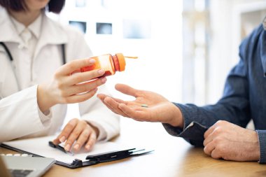 Modern poliklinikteki hastaların eline turuncu şişeden tablet döken esmer doktorları kapatın. Hastalık ve acı belirtilerini azaltmak için ilaç alan bir erkek. Sağlık ve tedavi kavramı.