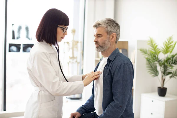 Pandangan Samping Wanita Terfokus Dalam Mantel Putih Menggunakan Stetoskop Sementara — Stok Foto