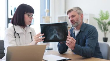 Kafkasyalı neşeli doktor ve hasta ellerinin röntgenini tutuyor ve modern hastanenin parlak kabinesindeki yapısal değişiklikleri inceliyor. Kayıt yapmak için taşınabilir dizüstü bilgisayar kullanan bir tıp çalışanı..