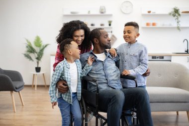 Çok kültürlü yetişkinler ve eğlenceli çocuklar hafta sonu boyunca geniş bir apartman dairesinde kalıyorlar. Neşeli oğullar okulda başarılı olmaktan bahsediyorlar. Gülümseyen anne ve babaya tekerlekli sandalyede..