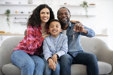 Oğulları kameraya gülümserken güzel, çok kültürlü bir anne kocasını evinin anahtarlarıyla kucaklıyor. Genç eşler ve çocuklar yeni bir konaklama yeri satın aldıktan sonra sevinçten kahroluyorlar..