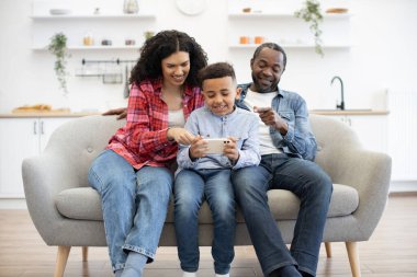 Meraklı çift, dinlenme odasındaki kanepede dinlenirken küçük sakin bir çocuğun tuttuğu parmakları ekranı işaret ediyor. Lezzetli bir yemekten sonra çevrimiçi video oyunu hakkında tavsiye veren yardımsever aileler..