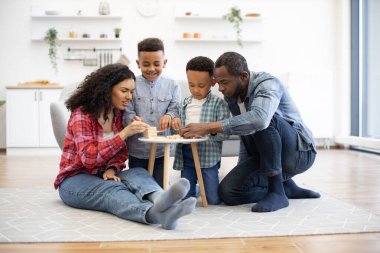 Çok ırklı dost canlısı aile öğle vakti kahve masasının etrafında toplanıyor. Mutlu çocuklar ve ilgili aileler mutfak zeminine tahta bloklardan yüksek bir kule inşa ediyorlar..
