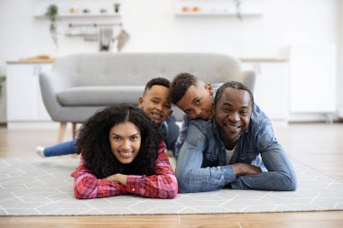 Neşeli, çok kültürlü anne ve baba içeride yerde yatarken mutlu çocukları sırtlarında taşıyorlar. Aktif ebeveynler spordan zevk alırken oğlanlar yaratıcı eğleniyor..