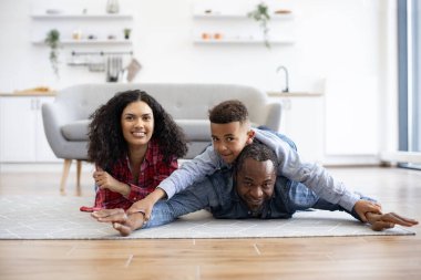 Sağlıklı afro-amerikan babası, güzel karısıyla mutfak zemininde otururken oğlunu geride tutuyor. Sevecen baba meraklı çocuğa yüzme stili gösterirken anne mutlu bir şekilde gülümsüyor..