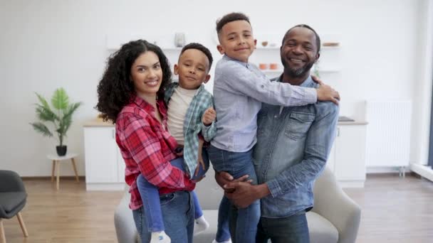 アフリカ系アメリカ人の配偶者の肖像画は 屋内で快適に感じながら 腕の中でよく振る舞った子供を保持する アパートで息子と楽しい活動を計画している家族の男と妻を愛する — ストック動画