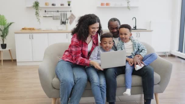 有爱心的非洲裔美国妈妈爱抚一个可爱的儿子 而快乐的爸爸则给另一个男孩看视频 快乐的父母和孩子们在家里玩的开心的同时用无线笔记本电脑 — 图库视频影像