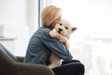 Kot gömlekli neşeli beyaz bayanın evde dinlenirken yumuşak köpek ceketi giydiği yakın bir manzara. Gülümseyen genç evcil hayvan sevdalısı şefkatle ve küçük teriyerle boğulmuş..