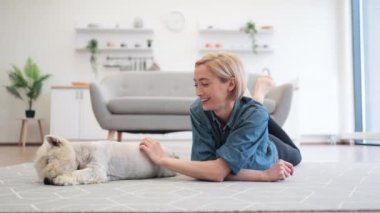 Geniş evdeki teriyerin yanında yerde yatarken köpek kürkünü inceleyen yetişkin bir kadın. Tarz sahibi genç evcil hayvan sahibi sevgili köpek arkadaşı için tımar günü planlıyor..