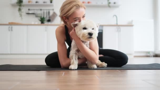 Affectionate Adult Female Yoga Activewear Embracing White Terrier While Sitting — Stock Video