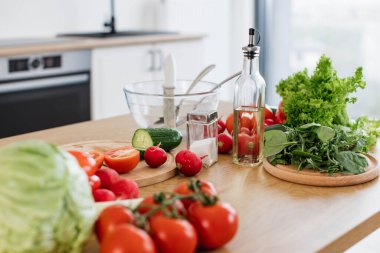 Mutfak masasında çatal bıçak seti ve kesme tahtasının yanına bırakılmış çeşitli çiğ sebzeleri ve yapraklı marulları yakından izleyin. Klasik soslu ev yapımı salata için doğal malzemeler kullanıma hazır..