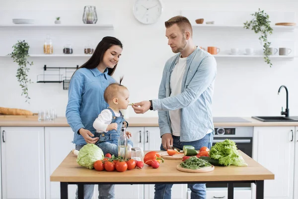 Healthy fit father in cozy clothes giving daughter fresh vegetable while preparing mixture salad for sunday brunch. Mindful spouse following recipe instructions during various stages of preparation.