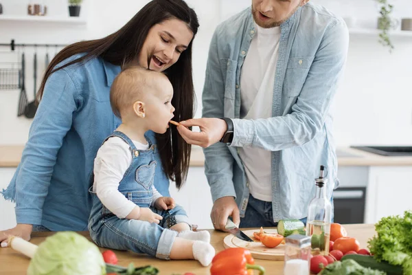 在现代厨房里 与可爱的女婴亲密接触 细细品味着慈祥的父母送给她的多汁蔬菜 快乐的高加索家庭在家庭内部享用健康的晚餐 — 图库照片