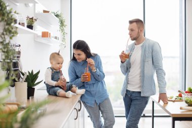 Baba, anne ve bebek mutfakta vakit geçiriyorlar ve besleyici kahvaltıdan sonra lezzetli vitamin sıvıları tüketiyorlar. Neşeli insanlar hafta sonu birlikte iyi dinleniyorlar..