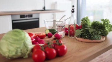 Mutfak masasında çatal bıçak seti ve kesme tahtasının yanına bırakılmış çeşitli çiğ sebzeleri ve yapraklı marulları yakından izleyin. Klasik soslu ev yapımı salata için doğal malzemeler kullanıma hazır..