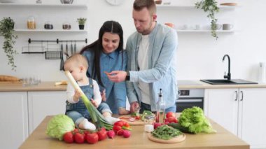 Mutlu bir aile babası, küçük kızını beslerken bir yandan da gülümseyen bir anne, mutfak sandalyesinde oturmuş, küçük kıza tezahürat yapıyor. Genç eşler tatlı domates ikram ederek çocuk diyetine yeni besinler ekliyorlar..