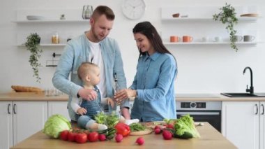Güzel esmer kadın kase içine sebzeler ve sebzelerle sıvı dökerken küçük kız da şişeye yardım ediyor. Mutfakta birlikte çalışırken arkadaş canlısı genç bir aile paylaşımı ve bağ kurma..