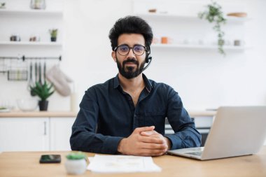Mikrofonlu, belgeli ve taşınabilir bilgisayarlı gülümseyen insan portresi. Neşeli Arap danışmanı müşterilerine dijital platformdan rehberlik sunuyor..