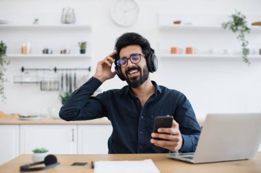 Gözlüklü rahat bir Arap, içerideki kablosuz cihazlar aracılığıyla gelen seslere büyük bir ilgi gösteriyor. Gerçek müzik aşığı kulaklıktaki saf performansın tadını çıkarıyor..