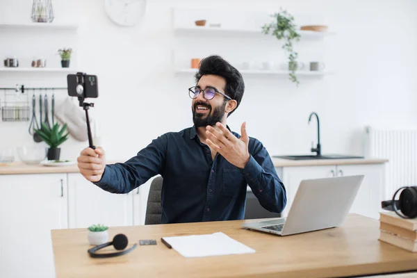 Vidám Arab Felnőtt Szemüvegben Állványt Tart Okostelefonnal Miközben Íróasztalnál Dolgozik — Stock Fotó