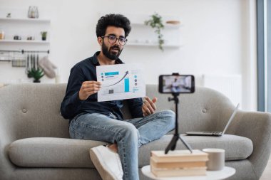 Hevesli bir Arap okutmanı gözlüklü cep telefonundaki video bağlantısıyla finansal okuryazarlığı öğretiyor. Zeki profesör canlı yayın sırasında öğrencilere para birimi büyüme grafiği gösteriyor.