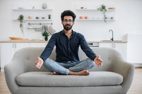 Mutfak arka planındaki yumuşak koltukta rahat bir şekilde dinlenen gülümseyen Arap beyefendinin portresi. Rahatlamış yetişkin göz giysisi sağlıklı yaşam tarzını meditasyon yoluyla destekliyor..